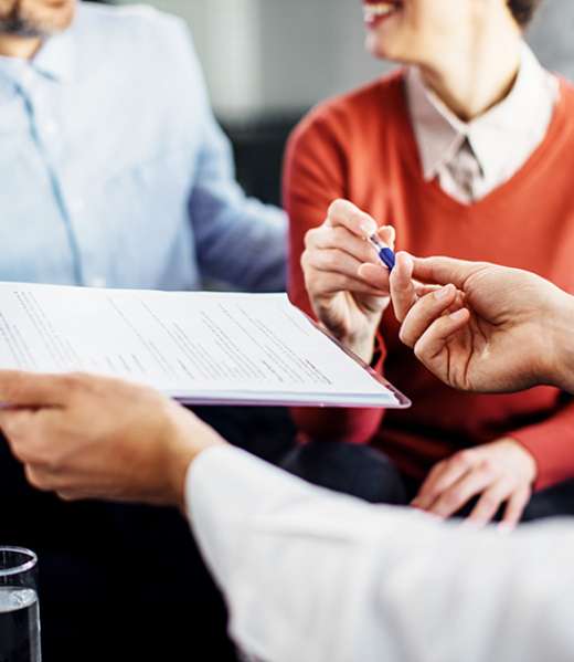 Close-up of woman signing an agreement with insurance agent while being on a meeting with her husband.